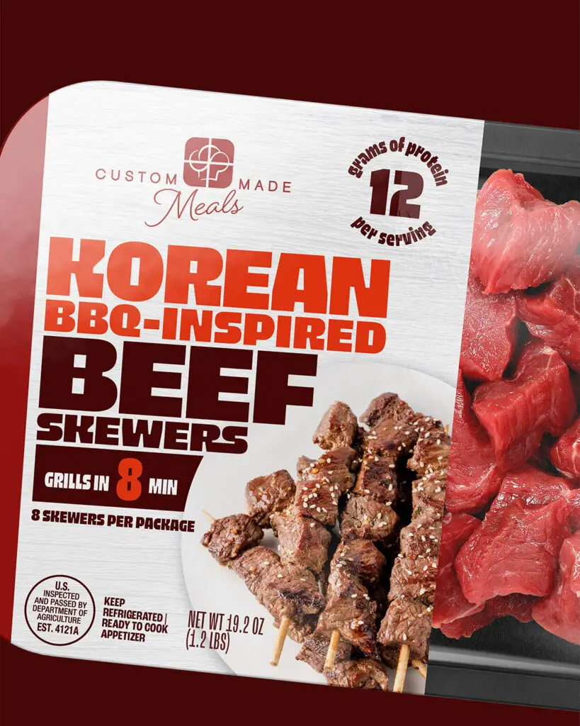 A tray of Korean BBQ-Inspired Beef Skewers, by Custom Made Meals, with red and brown text and picture of prepared skewers on a tan background.