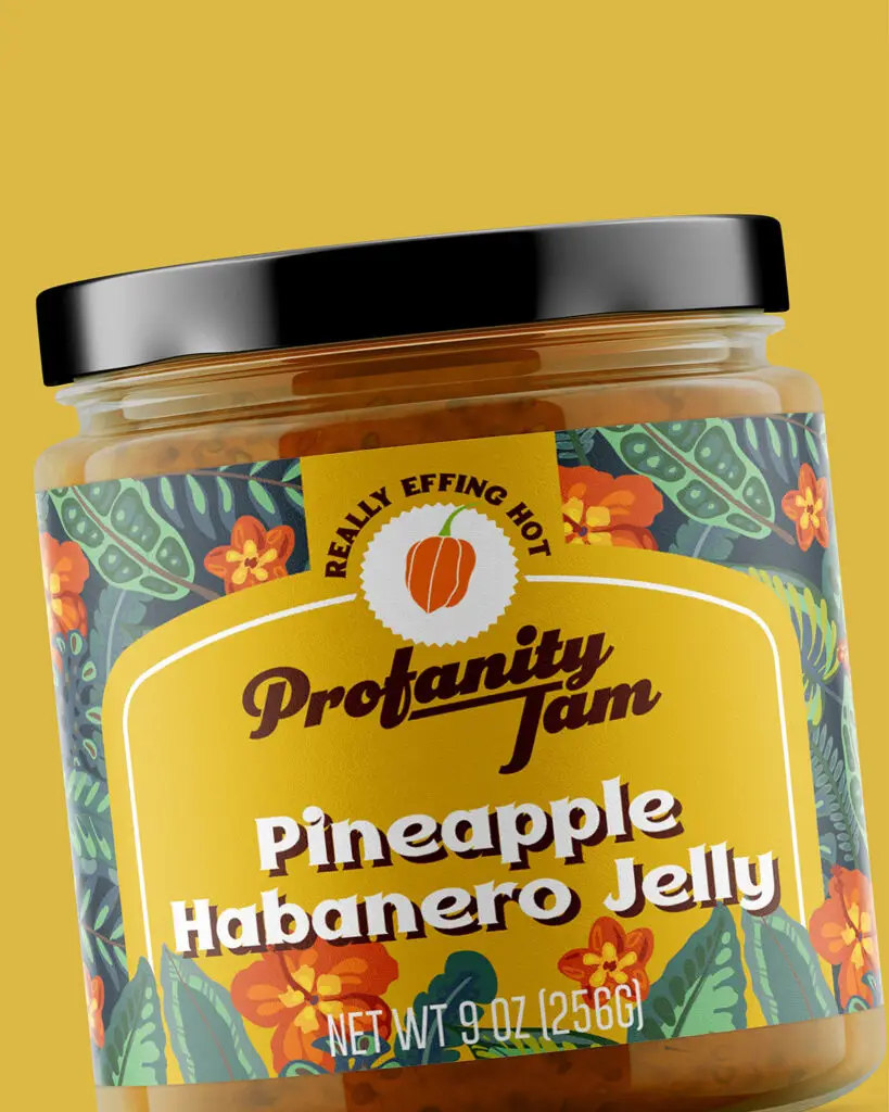 A 9oz jar of Profanity Jam's Pineapple Habanero Jelly, with brown and white text and green/orange designs on a gold background.